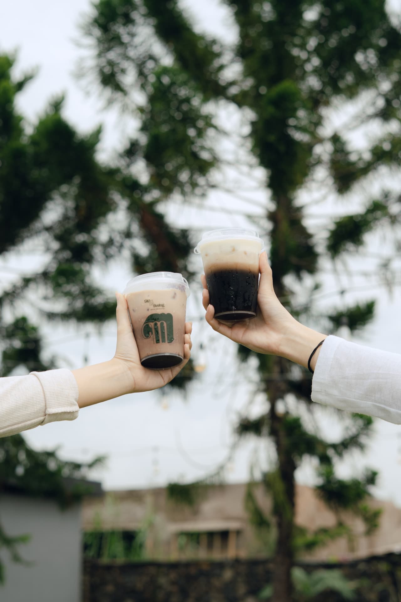 Dua tangan bersulang dengan kopi dingin Magnolia di area terbuka